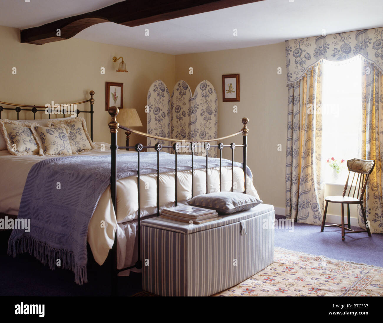 Ottoman rayé ci-dessous lit en cuivre avec jet bleu pâle en pays chambre avec toile blanc +bleu-de-Jouy paravent et rideaux Banque D'Images