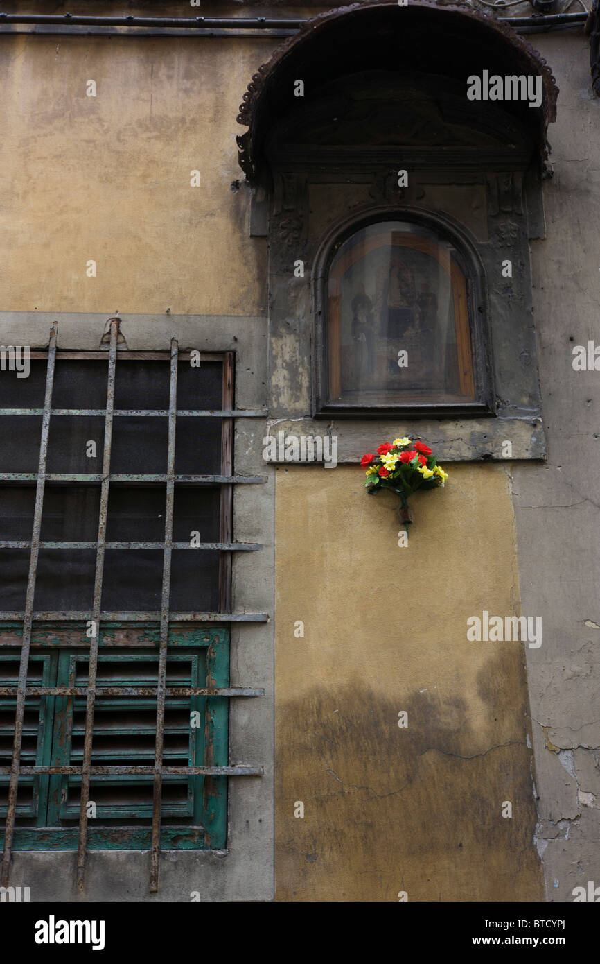 Couleurs vives de fleurs en plastique bouquet sous miteux et religieux en décomposition murale sur mur de Florence. Banque D'Images