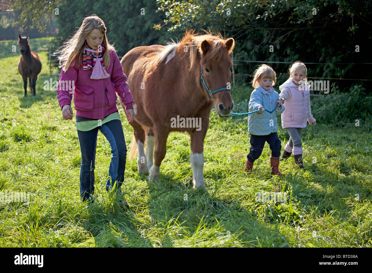 Deux petites filles à la tête d'un big pony supervisé par une adolescente Banque D'Images