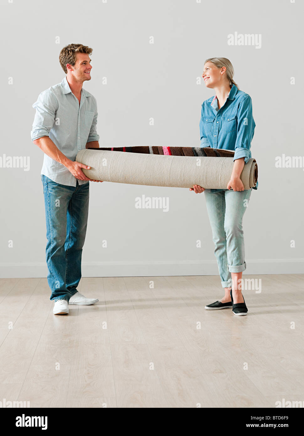 Jeune couple carrying a rolled up rug Banque D'Images