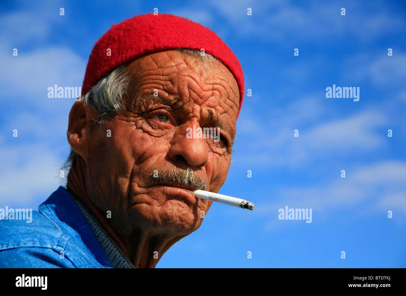 Portrait d'un vieux pêcheur musulmane avec visage ravagé et fez rouge, fumer une cigarette Banque D'Images