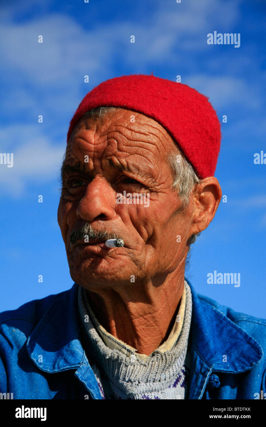 Portrait d'un vieux pêcheur musulmane avec visage ravagé et fez rouge, fumer une cigarette Banque D'Images