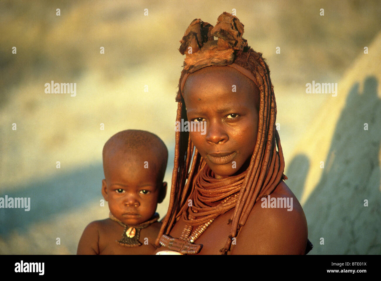 Himba mère avec son enfant sur la hanche avec ses cheveux et corps couvert en ocre rouge Banque D'Images