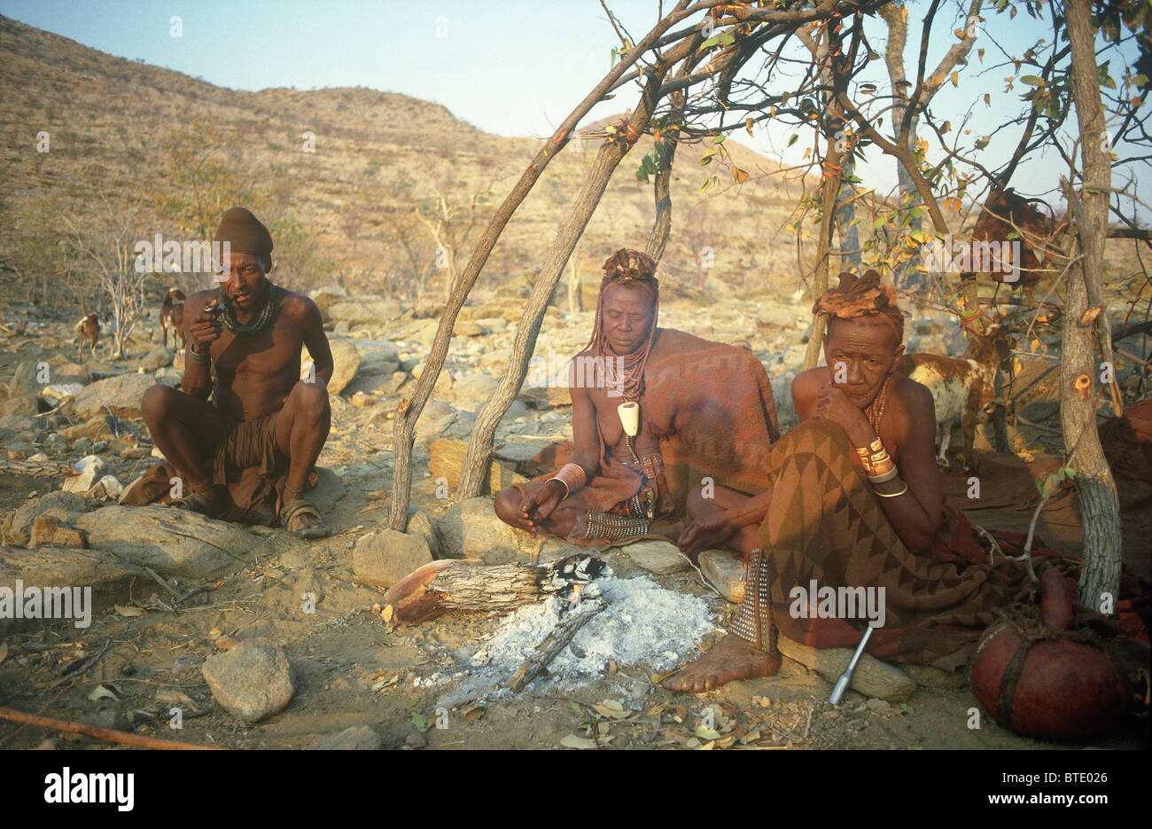Homme Himba et deux femmes âgées assis près de la cendre d'un feu Banque D'Images