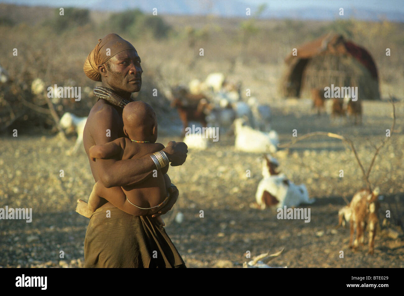 Himba homme portant un bébé sur la hanche près de son homestead Banque D'Images