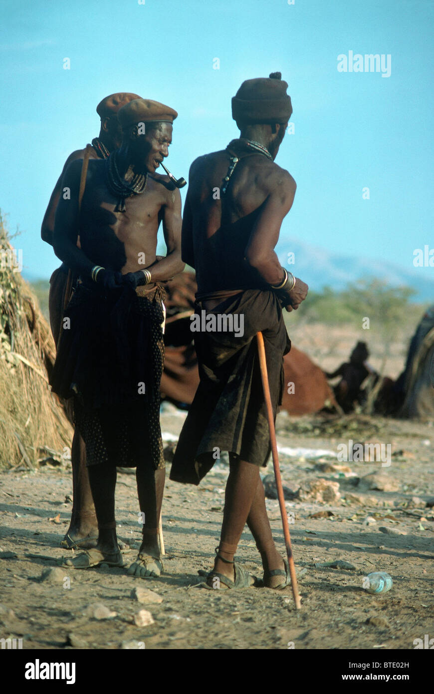 Himba trois hommes debout ensemble, l'une appuyée sur un bâton de marche près de leur propriété Banque D'Images