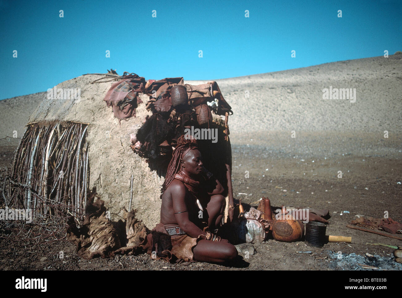 Une femme Himba assis devant sa hutte traditionnelle Banque D'Images