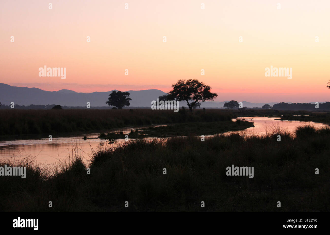 Coucher de soleil avec en premier plan la rivière Zambèze et la montagne et les arbres en arrière-plan Banque D'Images