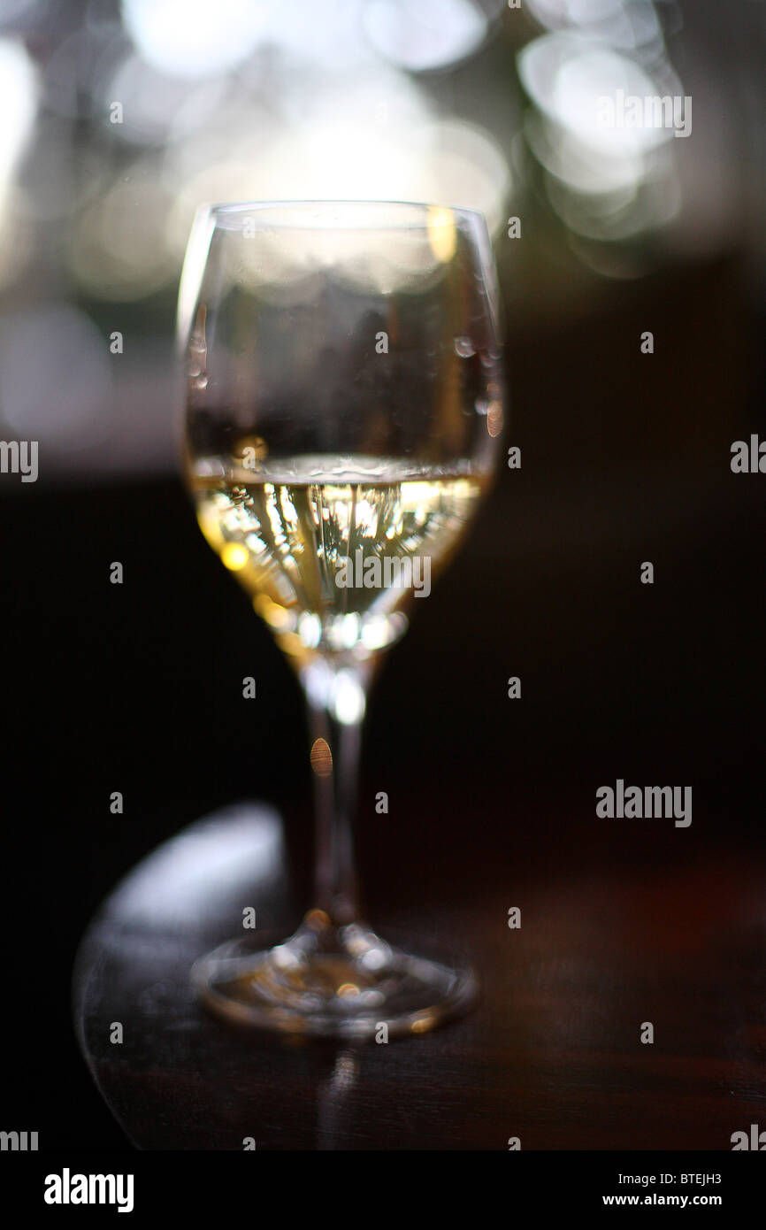 Vin blanc dans un verre de vin rond rempli d'un tiers sur le bord d'une table ronde en bois avec arrière-plan flou Banque D'Images