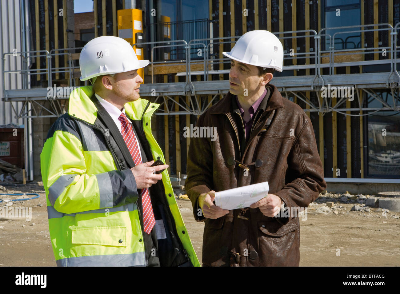 Businessman in hard hat et des vêtements réfléchissants de parler à entrepreneur en construction Banque D'Images
