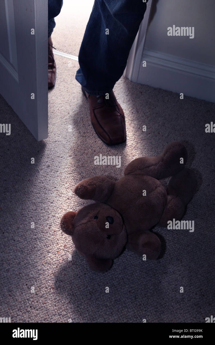 Ours en peluche de l'enfant allongé sur le sol d'une chambre dotée de moquette que celui d'un homme dans l'étape pieds à travers une porte ouverte Banque D'Images