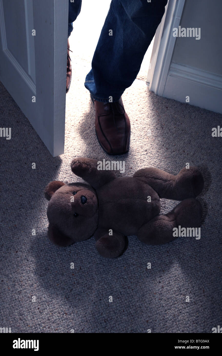 Ours en peluche de l'enfant allongé sur le sol d'une chambre dotée de moquette que celui d'un homme dans l'étape pieds à travers une porte ouverte Banque D'Images