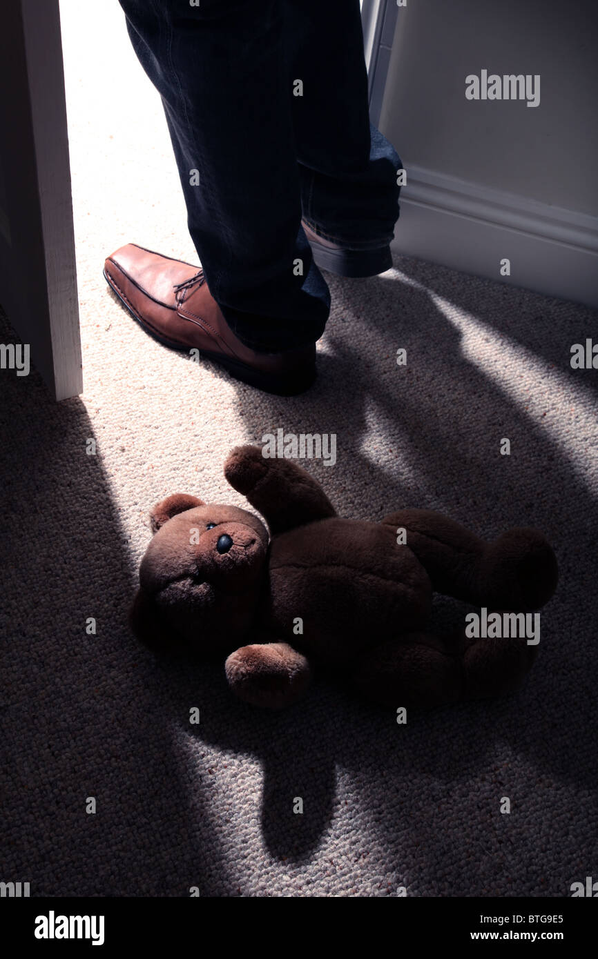 Man (pieds et jambes uniquement) Le port de chaussures brunes enjambant un ours allongé sur le sol par une porte ouverte. Banque D'Images