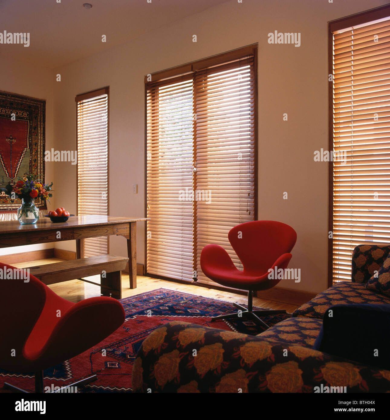 Stores en bois à lattes sur de grandes fenêtres dans le salon et la salle à manger moderne avec Arne Jacobsen 'rouge' 'Swan' chaise et canapé à motifs Banque D'Images