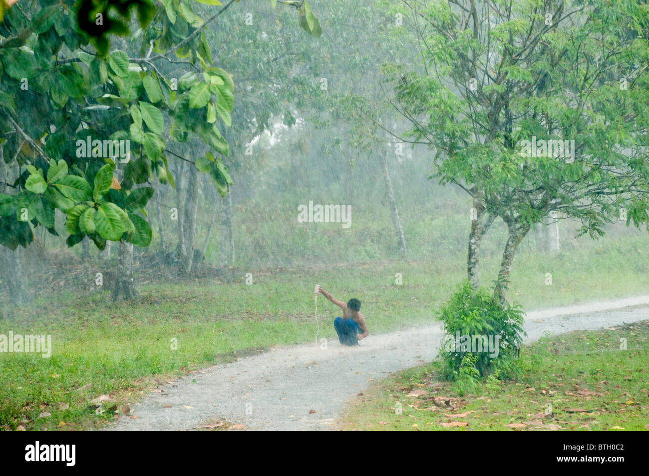 Garçon jouant dans une flaque d'eau au cours d'une averse tropicale près de Sukau B&B par Sungai Kinabatangan à Bornéo Banque D'Images