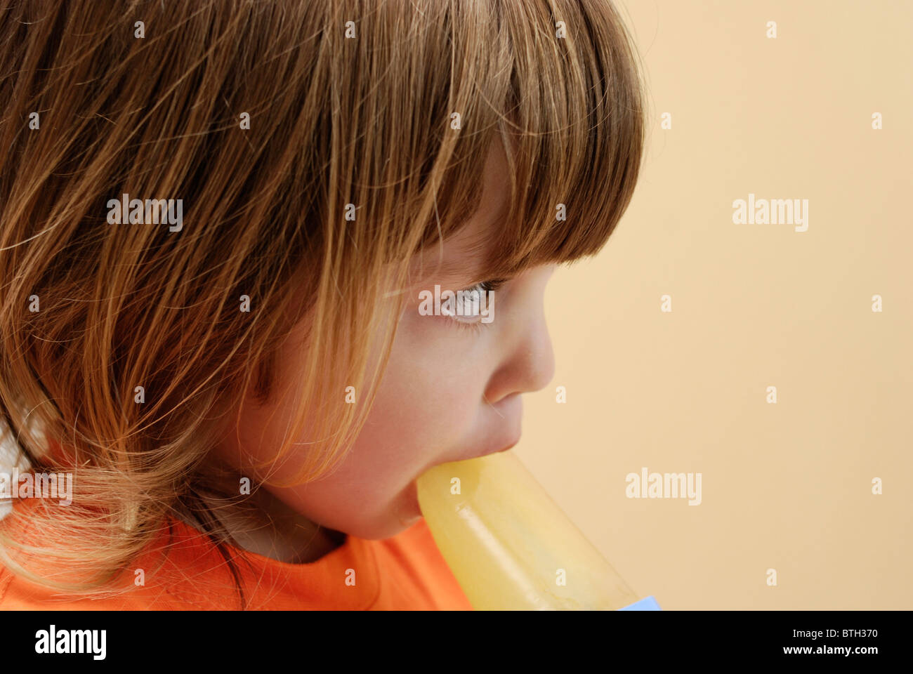 Trois ans, fille de manger une orange ice lolly. Banque D'Images