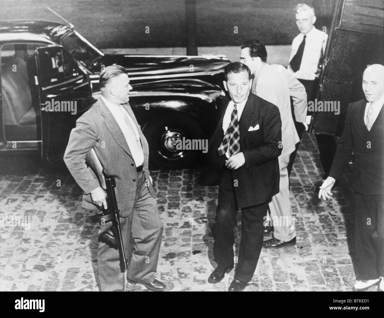 'Louis Lepke Buchalter' (1897-1944), en arrivant à la Cour d'appel d'Albany, New York seulement pour entendre sa condamnation à mort confirmée. Il fut exécuté le 4 mars 1944. Détective Albany Joseph Nowak l'accompagne avec un Tommy gun. Le 20 juillet 1943. Banque D'Images