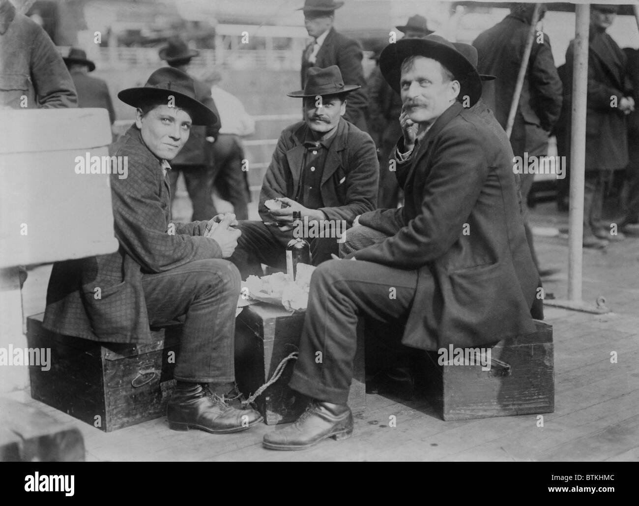 Trois hommes gais (probablement les Allemands), partager un repas et une bouteille sur le navire d'immigrants le président Grant de la ligne américaine de Hambourg à la fin de son voyage dans le port de New York. Ca. 1910. Banque D'Images