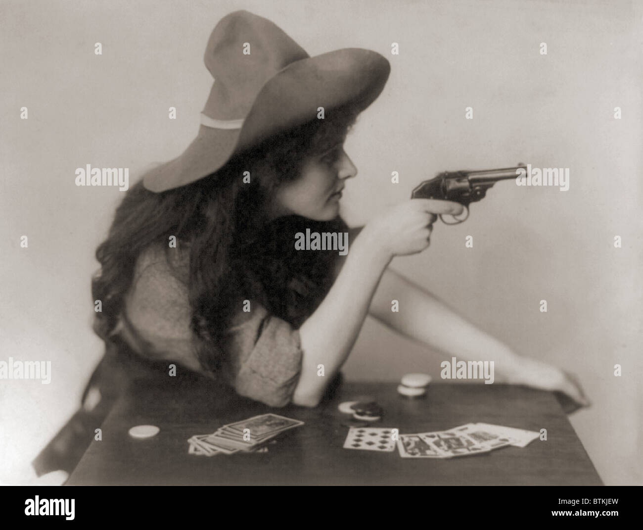 Cowgirl avec jeu de cartes et de jetons, pointant un pistolet. 1912. Banque D'Images