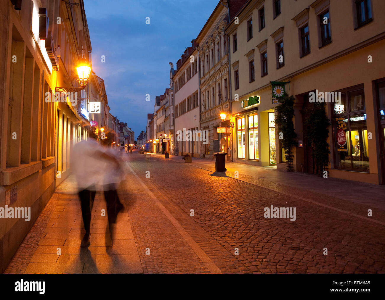 Un seul couple dans la nuit marche bras dessus bras dessous le long d'une rue pavée de Wittenberg, Allemagne. Banque D'Images