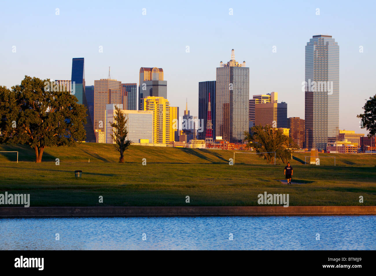 Un homme marche dans un parc à côté d'un lac avec le Dallas, TX skyline importante dans l'arrière-plan. Banque D'Images