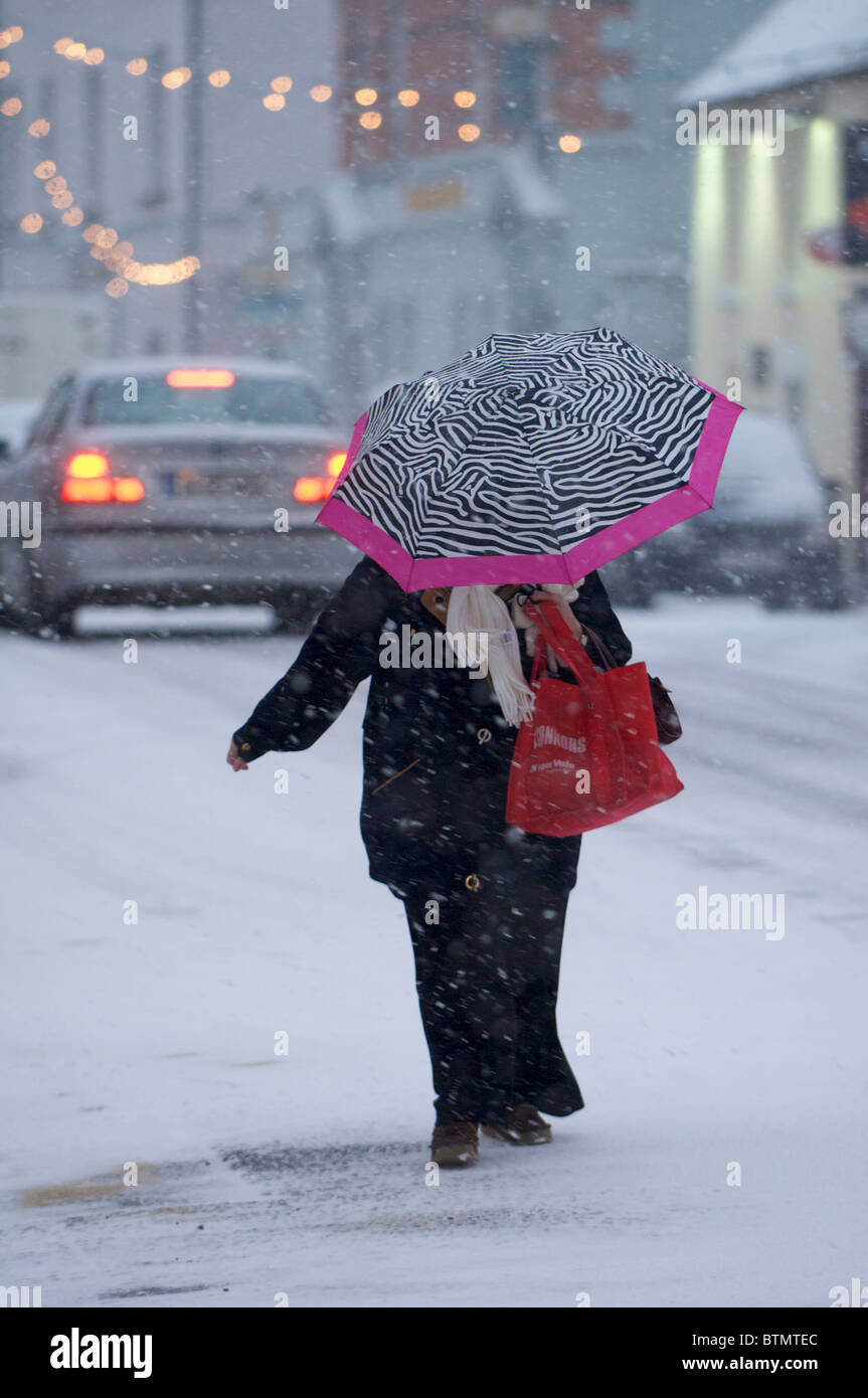 Une femme avec un parapluie traverse une rue au cours d'une averse de neige à Castlebar, Comté de Mayo, Irlande Banque D'Images