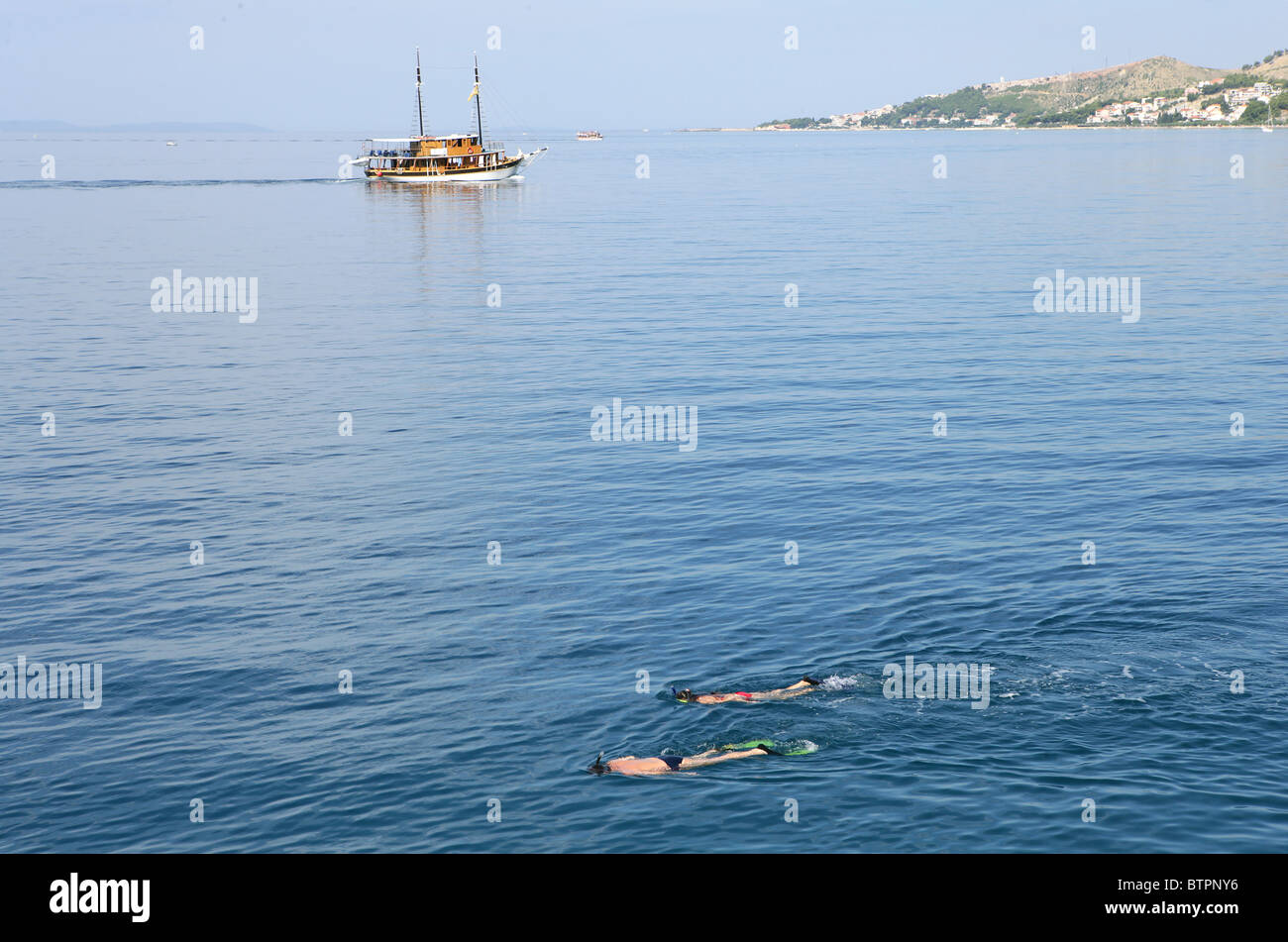 Les gens de la plongée dans les eaux claires de la mer Adriatique, tandis qu'un voile pases par près de la ville d'Omis, Croatie Banque D'Images