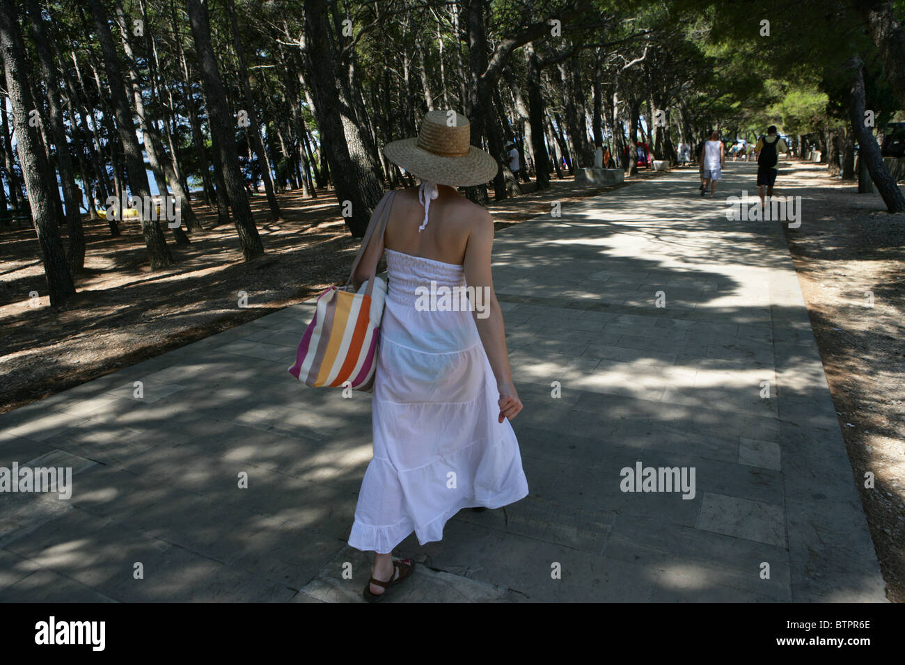 Une jeune femme se promène le long de l'avenue ombragée près de la plage à Bol, sur l'île de Brac, Croatie Banque D'Images