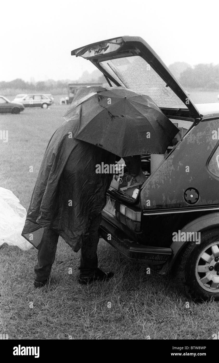 L'homme à l'abri de la pluie torrentielle comme il emballe ses affaires dans la voiture à un vide grenier Banque D'Images