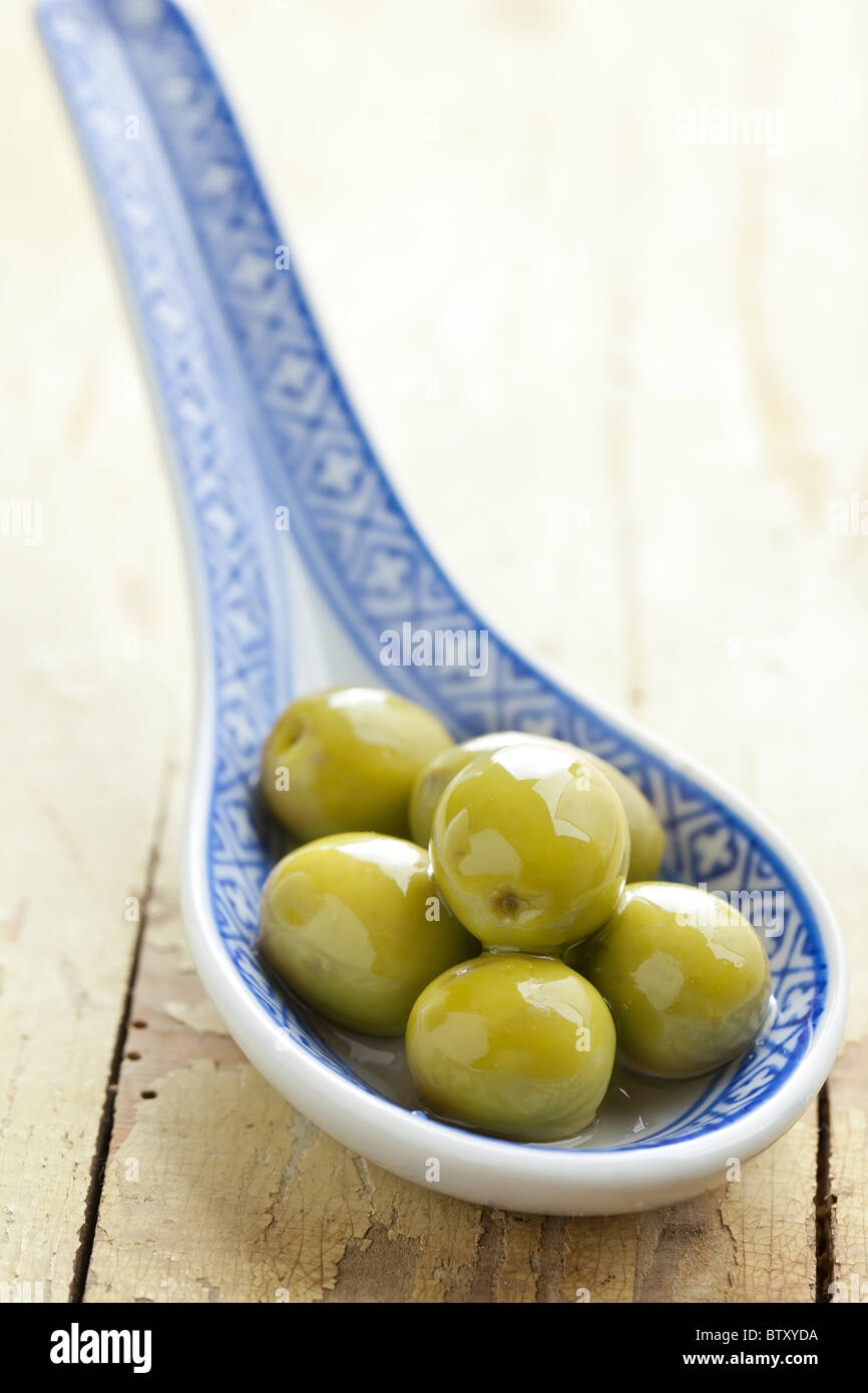 Les olives vertes en cuillère en céramique sur l'ancienne table Banque D'Images