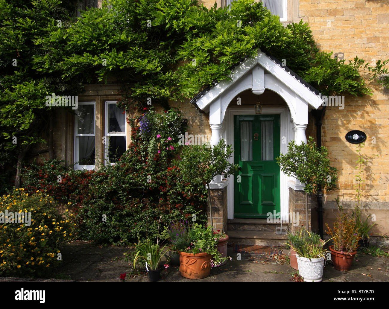 Entrée de maison en pierre, entourée de plantes en pots et de plus en plus à travers la porte de glycines, au-dessus du porche, vert. Banque D'Images