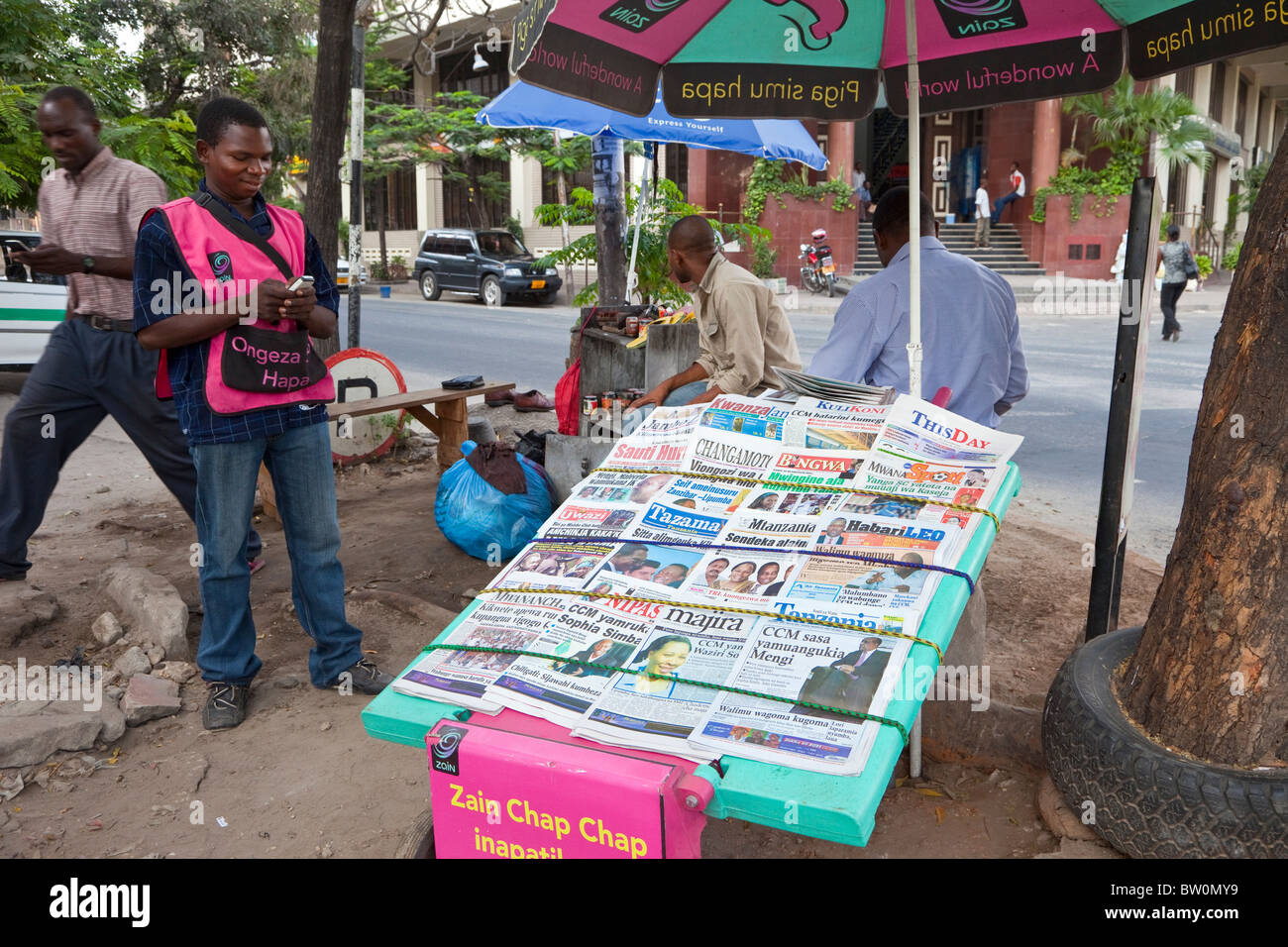 Dar es Salaam, Tanzanie. Vendeur de journaux contrôle de sa cellule téléphone (portable). La Tanzanie a de nombreux journaux de langue swahili. Banque D'Images