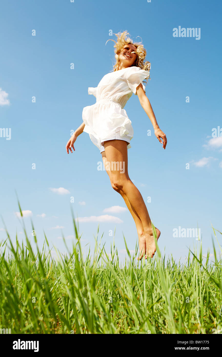 Photo de happy girl sautant par-dessus l'herbe verte sur journée d'été Banque D'Images