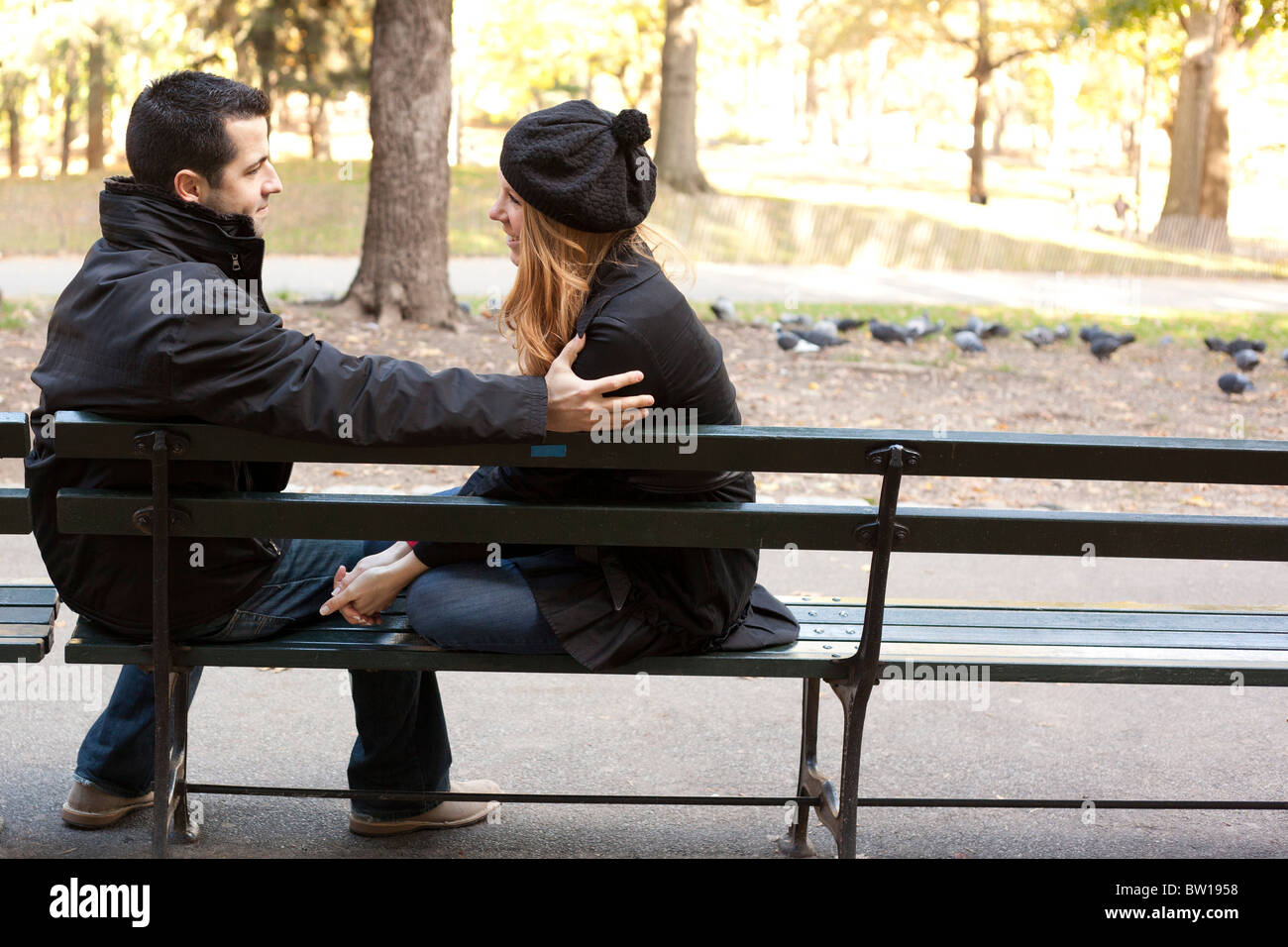 Un jeune couple assis sur un banc de parc au début de l'automne Banque D'Images