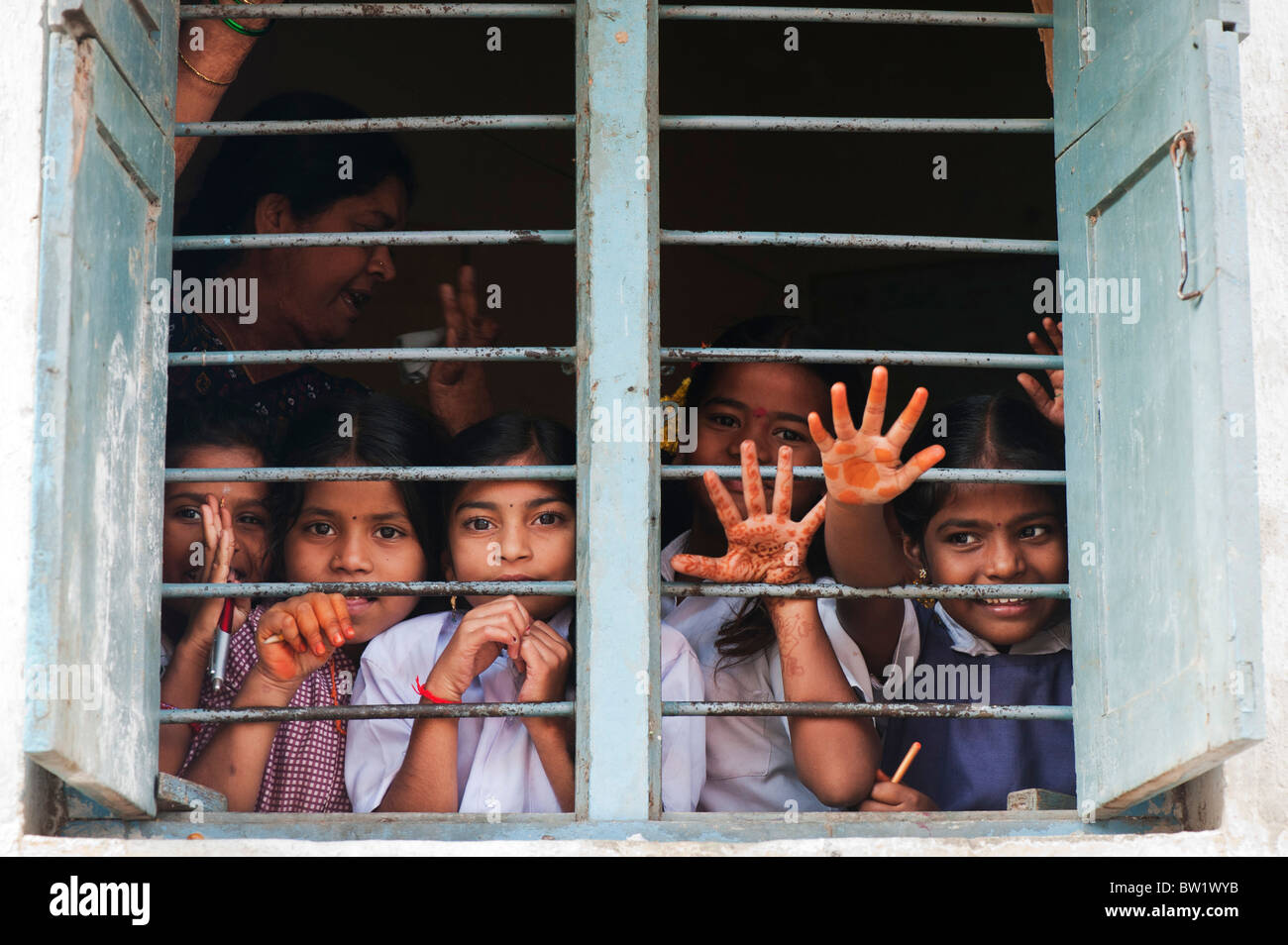 Les enfants de l'école du village de l'Inde et à la forme par l'intermédiaire de bars dans les fenêtres de leur école dans le vieux village de Puttaparthi. L'Andhra Pradesh, Inde Banque D'Images