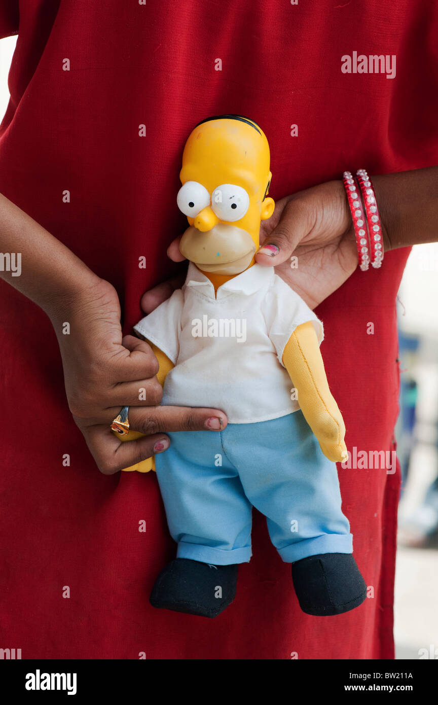 Jeune Indien street girl holding a Homer Simpson doll derrière son dos. L'Andhra Pradesh, Inde Banque D'Images