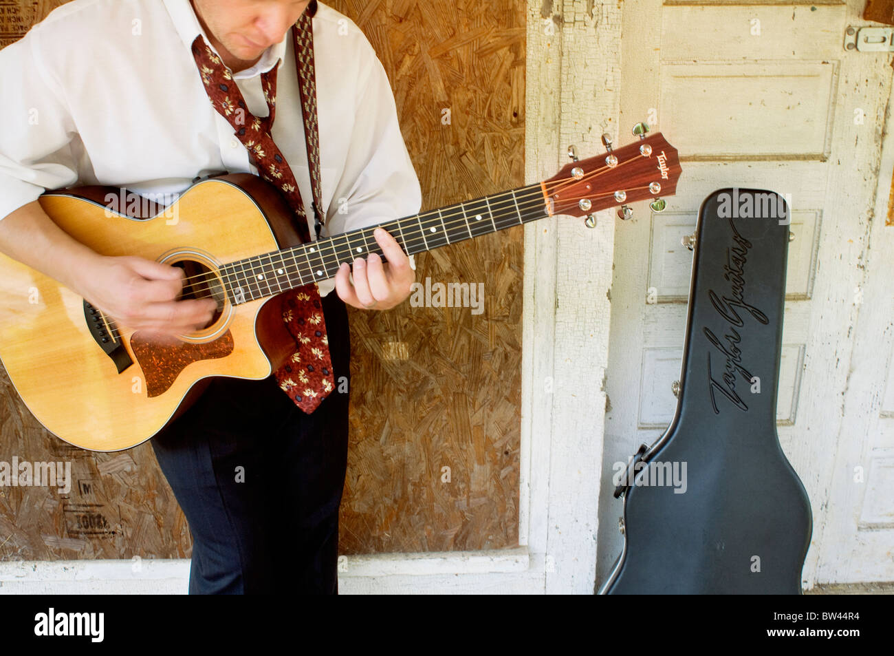 Un 38-year-old man jouer a guitare Taylor 314CE en dehors d'un run-down house Bynum, North Carolina, USA Banque D'Images