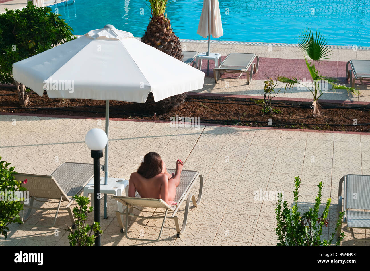 Une belle jeune fille nue bronzer nu sur un transat près de la piscine de  l'hôtel sous un parasol Photo Stock - Alamy