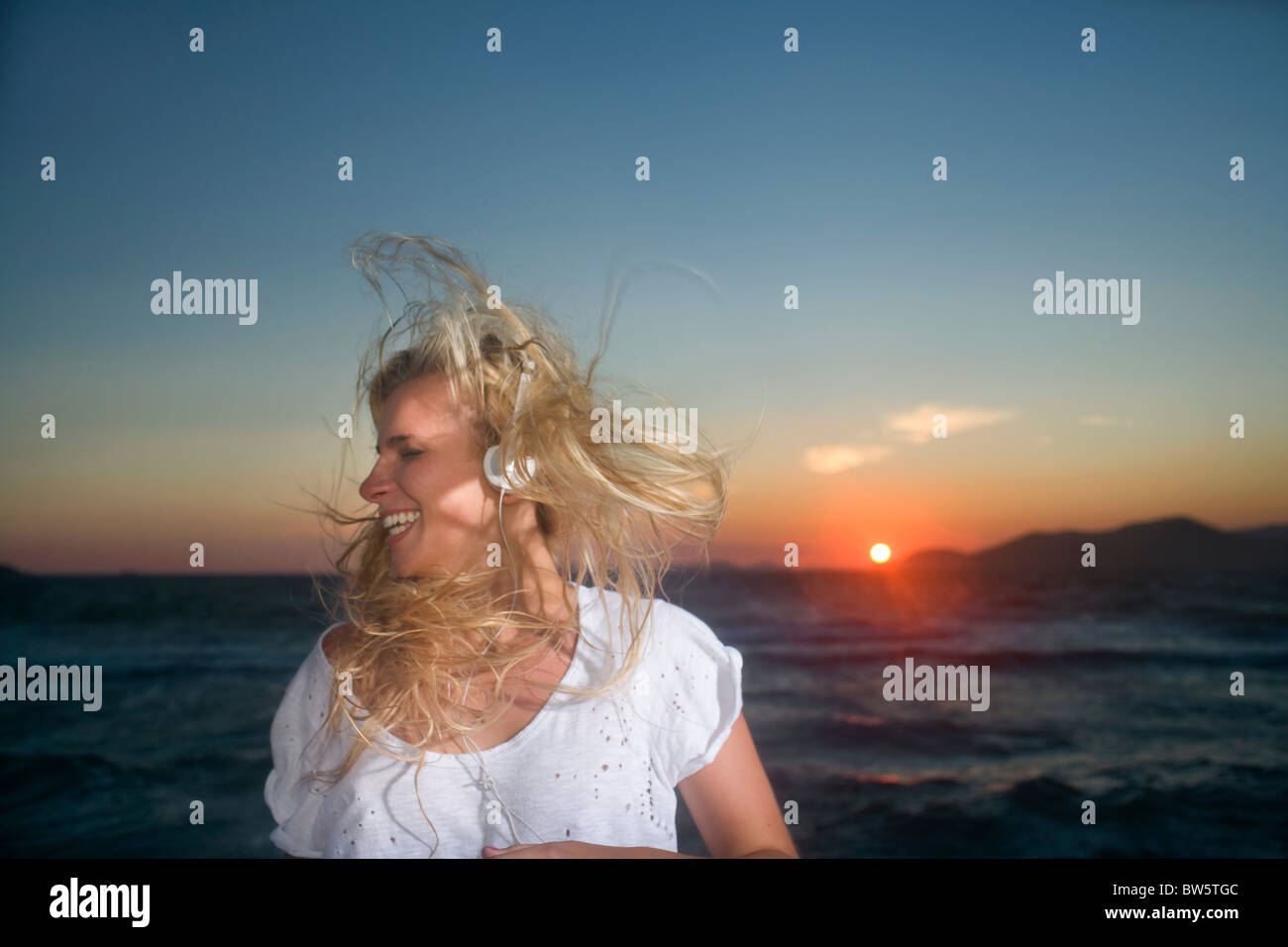 Jeune femme porte oreillettes au coucher du soleil Banque D'Images