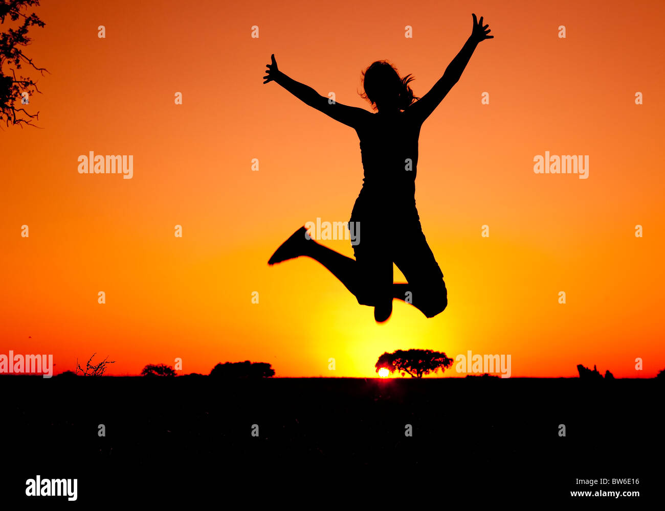 Silhouette d'une jeune femme sautant au coucher du soleil Banque D'Images
