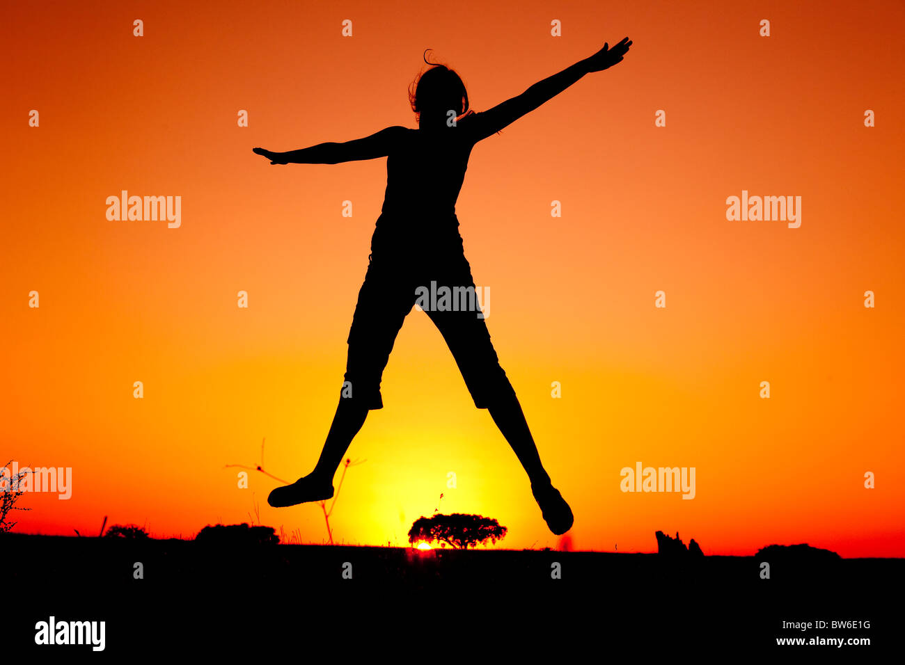 Silhouette d'une jeune femme sautant au coucher du soleil Banque D'Images