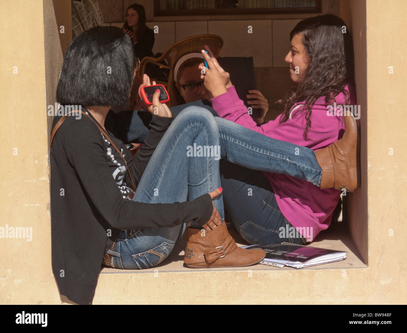 Les élèves à l'aide de téléphones portables assis sur mur, Université américaine du Caire, Egypte Banque D'Images