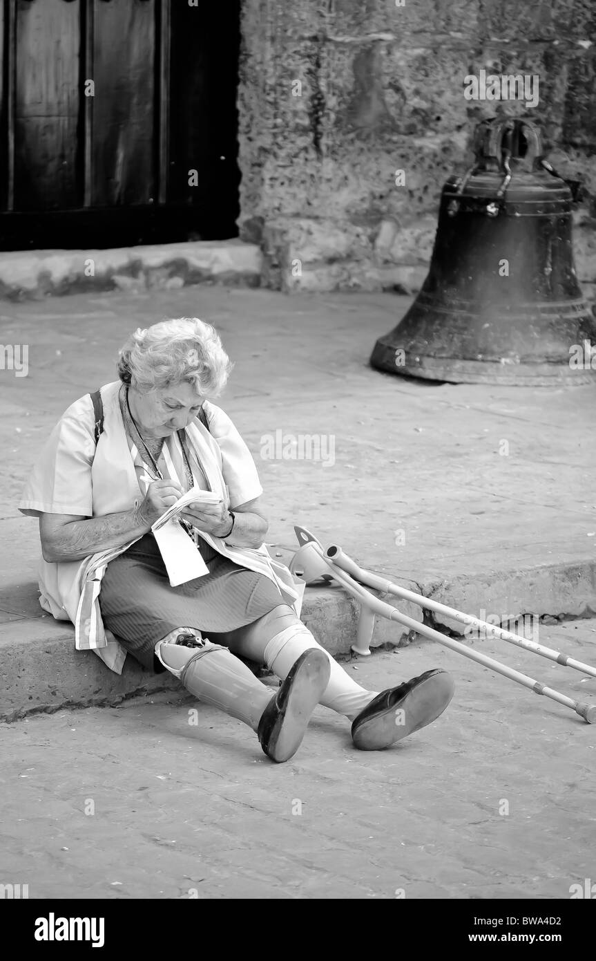 Une vieille dame avec un vieux exposés prothèse et béquilles assis à côté d'une église à La Havane, Cuba. Banque D'Images