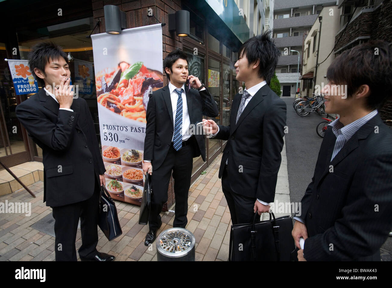 Les jeunes hommes fumeurs à l'extérieur d'un restaurant pendant leur pause déjeuner, Tokyo, Japon. Banque D'Images