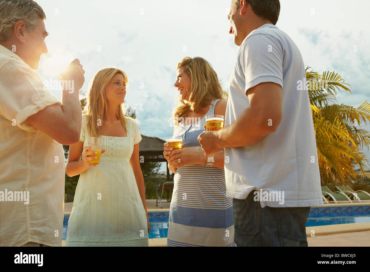 Groupe d'amis ayant des boissons près de la piscine Banque D'Images