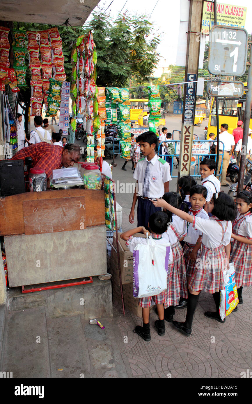 Les enfants de l'école indienne en uniforme se retrouvent autour d'une petite boutique sur la rue pour acheter des friandises avant d'aller à l'école, le Hyderabad Inde Banque D'Images