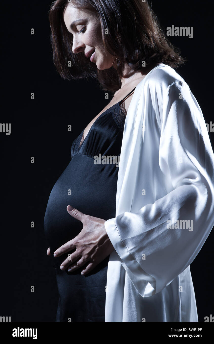 Beautiful smiling caucasian pregnant woman touching her belly portraitt nuisette en studio sur fond noir isolé Banque D'Images