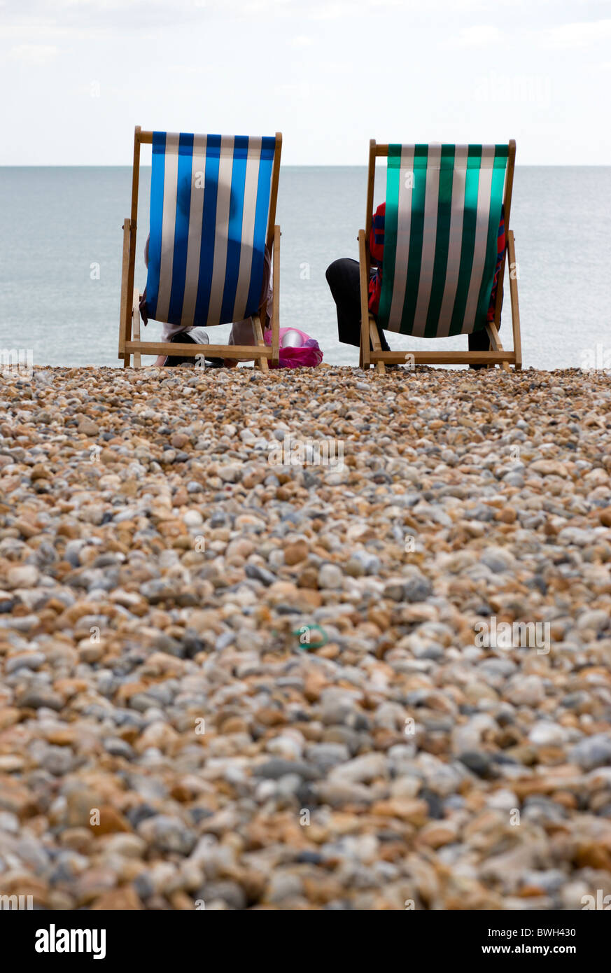 L'Angleterre, West Sussex, Bognor Regis, deux personnes âgées personnes âgées assis sur des transats sur la plage de galets face à la mer. Banque D'Images