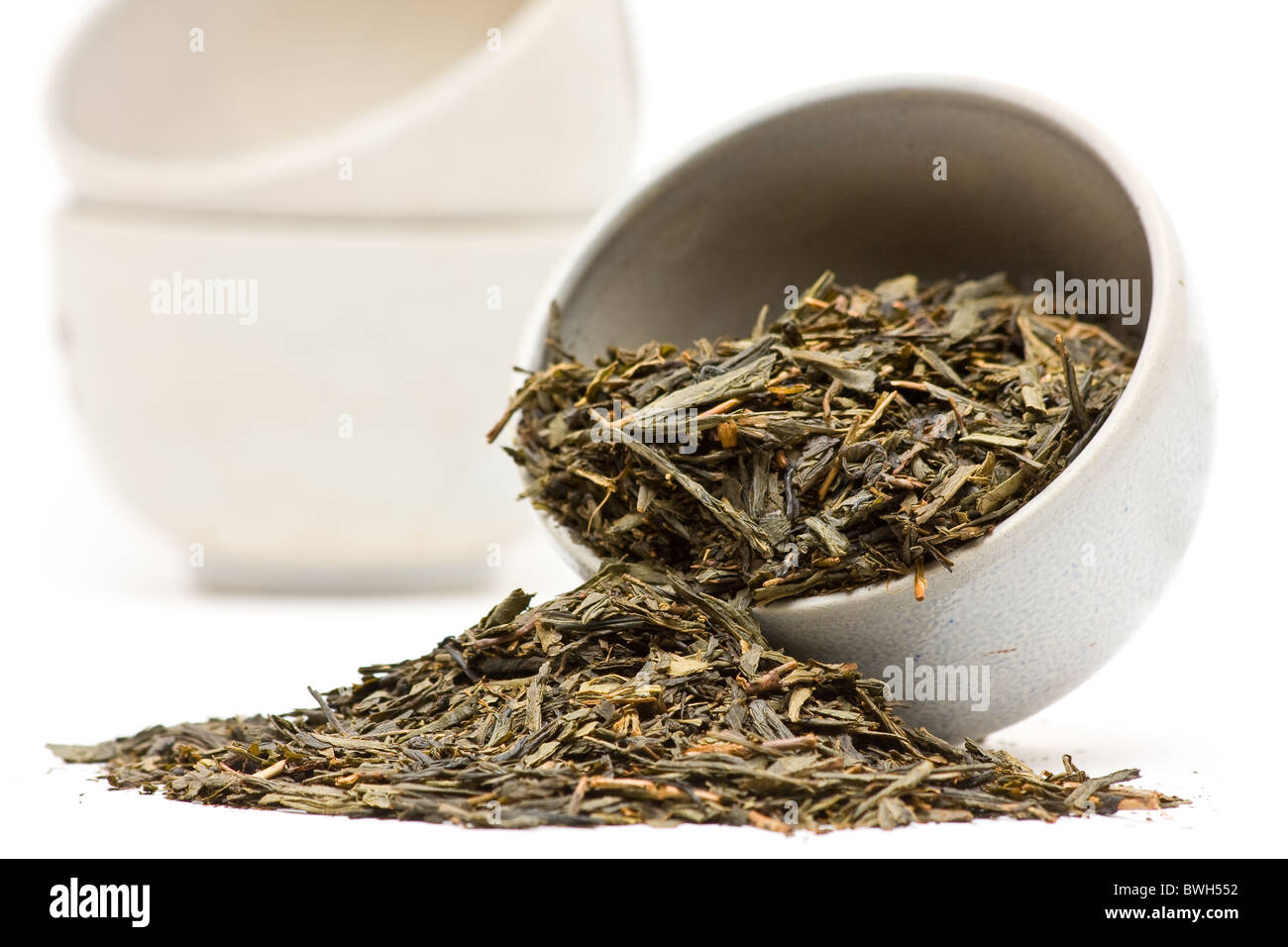 Feuilles de thé vert séchées dans la tasse en céramique sur fond blanc Banque D'Images