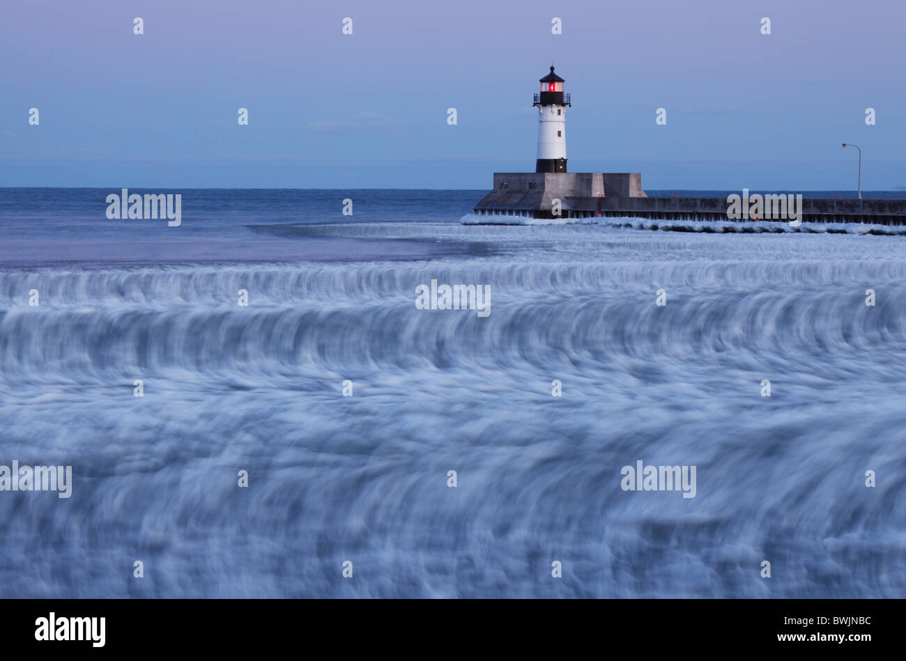 Vue d'hiver de phare au crépuscule à Duluth, MN montrant des blocs de glace sur le matériel roulant des vagues - faible vitesse d'obturation utilisée pour révéler le mouvement. Banque D'Images